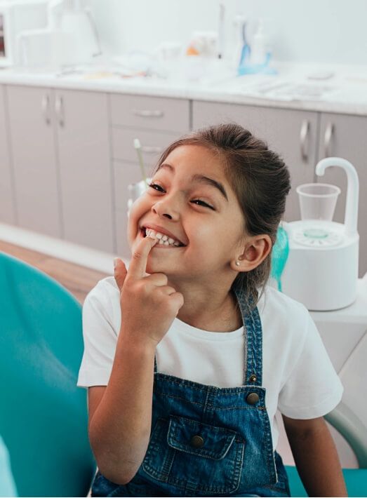 Young girl pointing to her smile during children's dentistry visit