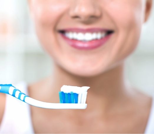 Person smiling in front of toothbrush with dab of toothpaste on it