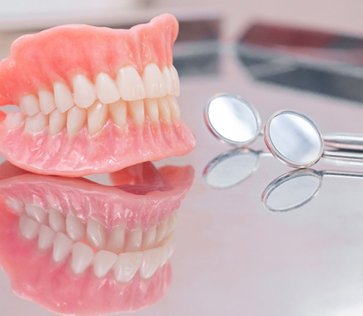 Complete set of dentures next to dental mirrors on reflective surface