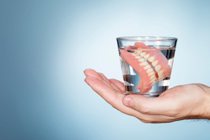 Hand holding glass with dentures in clear fluid