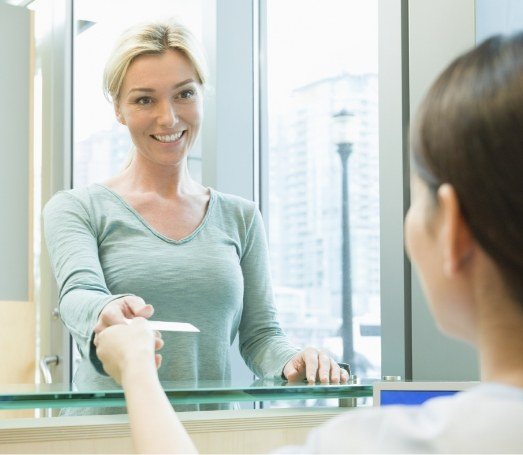 Woman handing payment card to dental team member at front desk