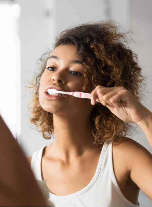 Woman brushing her teeth for cosmetic dentistry aftercare in Los Angeles