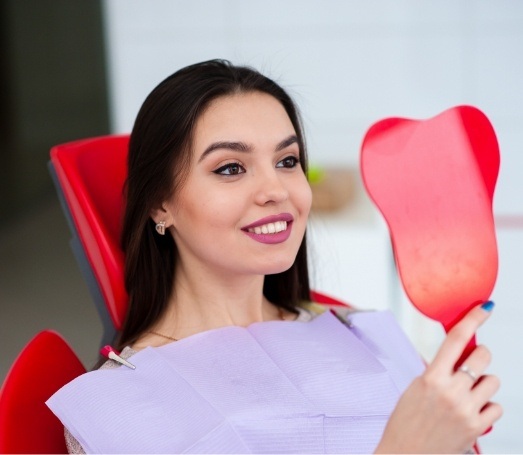 Woman looking at her smile in mirror after cosmetic dentistry