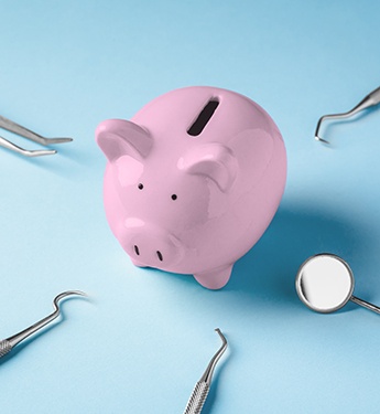A piggy bank surrounded by dental instruments on a blue background