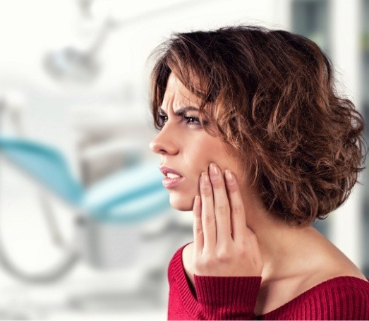 Woman in red sweater holding her jaw in pain