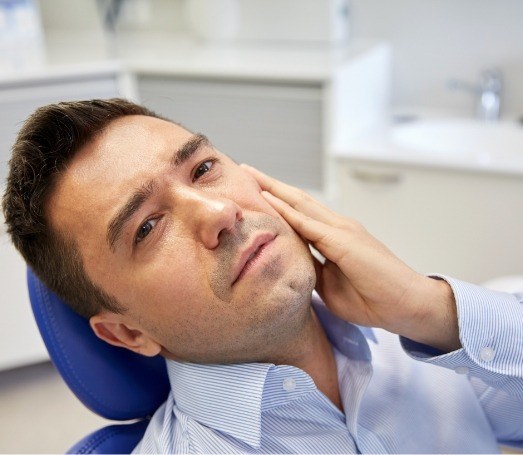 Man in dental chair holding the side of his mouth in pain