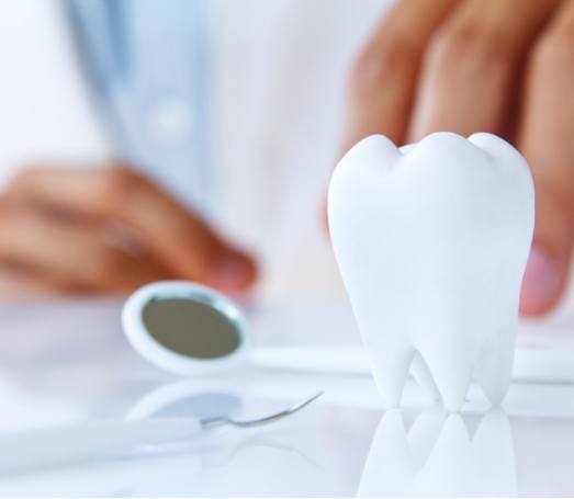 Model of tooth on desk next to dental mirror