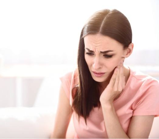 Woman in peach colored shirt holding her jaw in pain