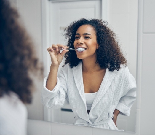 Woman in white bathrobe brushing her teeth