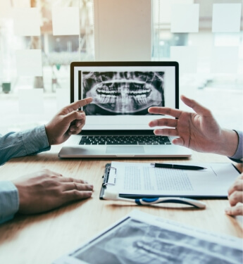 Two people talking at desk with laptop showing dental x rays