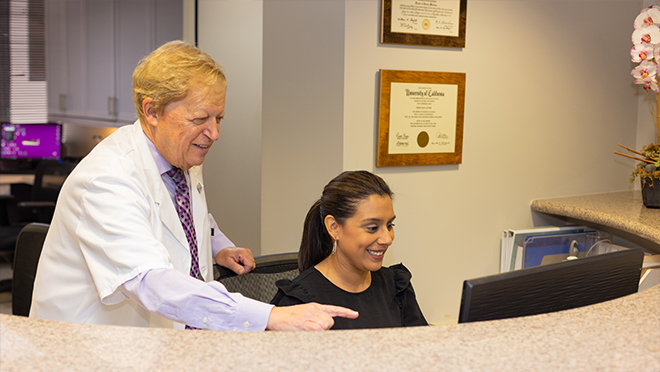 Doctor Latner looking at computer with dental team member at front desk