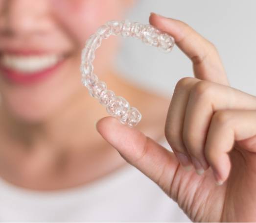 Smiling person holding Invisalign clear aligner