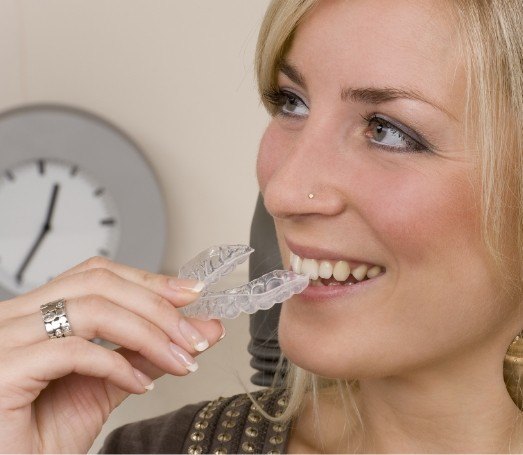 Blonde woman placing Invisalign aligner in her mouth