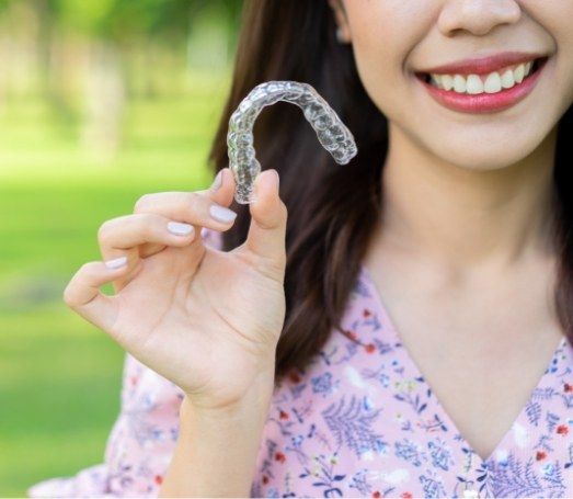 Smiling woman holding Invisalign aligner outdoors