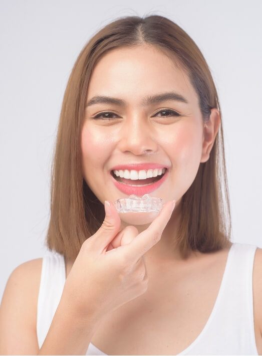 Smiling woman in white tanktop holding Invisalign in Los Angeles