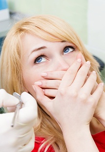 Scared woman in dental chair covering her mouth with her hands