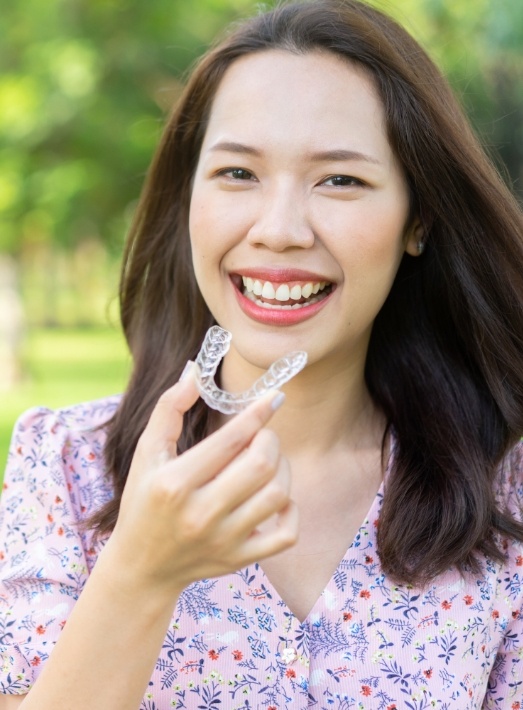 Smiling woman holding orthodontic aligner outdoors