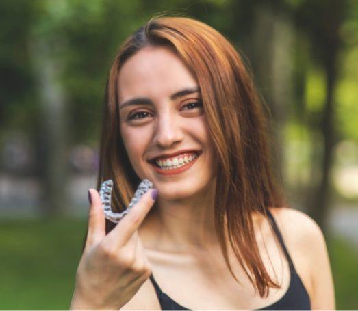 Young woman grinning and holding Invisalign clear aligner outdoors