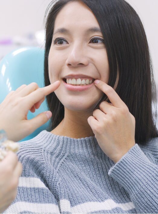 Woman in dental chair pointing to her new all porcelain dental crown in Los Angeles