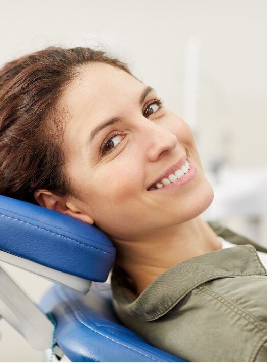 Smiling woman leaning back in dental chair after getting porcelain inlays and onlays