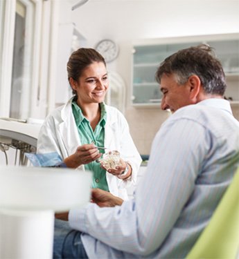 Smiling dentist showing patient model of teeth