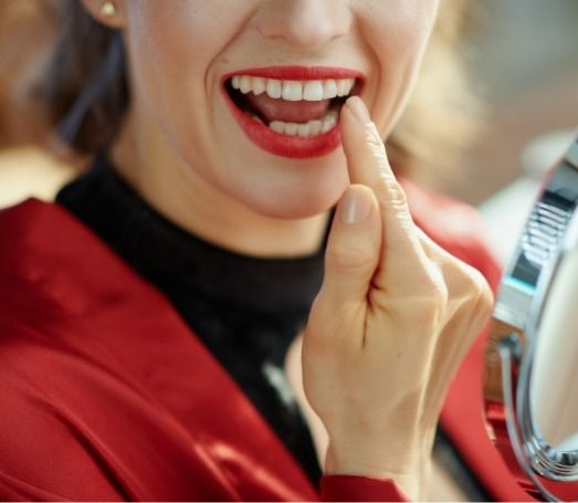 Woman with red lipstick looking at her teeth in mirror