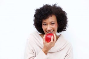 woman biting into a red apple after getting a full-mouth reconstruction in Los Angeles