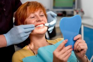 a woman smiling happily as her dentist examines her dental implants