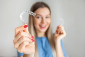 Smiling woman holding Invisalign aligner with manicured hand 